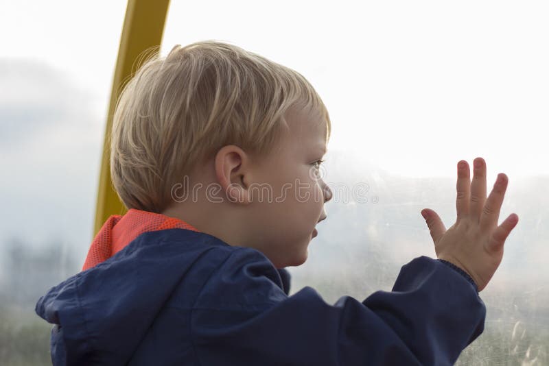 Peque?o muchacho rubio adorable del ni?o que se sienta cerca de ventana y que parece exterior fotografía de archivo libre de regalías Peque?o muchacho rubio adorable del ni?o que se sienta cerca de ventana y que parece exterior fotografía de archivo libre de regalías