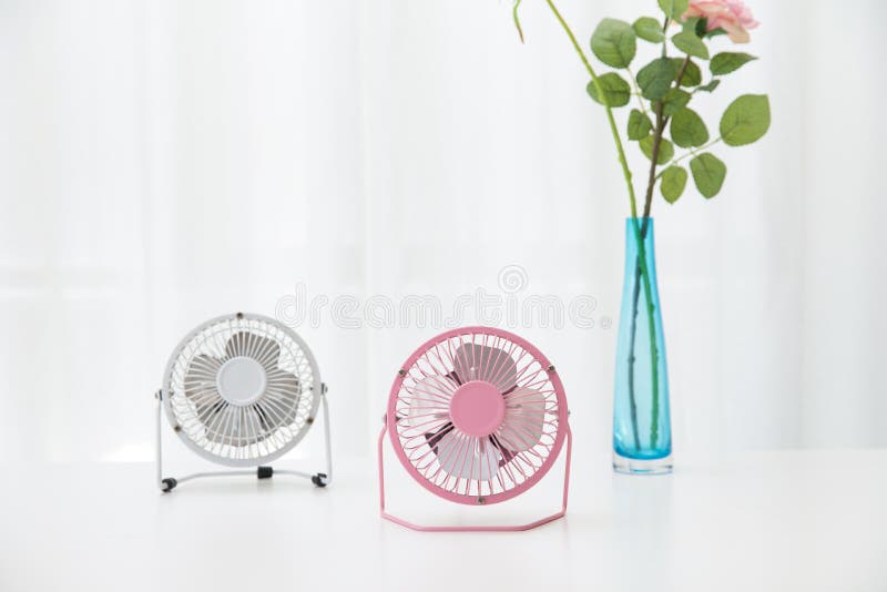 The small desk USB 4 blades cooling fans on a white table with roses in the background. The small desk USB 4 blades cooling fans on a white table with roses in the background