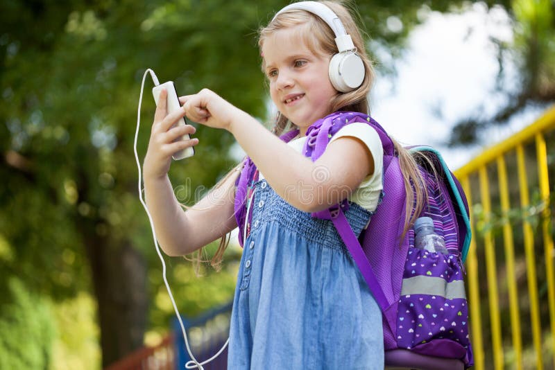 Pequeña colegiala linda que escucha la música afuera con blanco él imagen de archivo libre de regalías Pequeña colegiala linda que escucha la música afuera con blanco él imagen de archivo libre de regalías