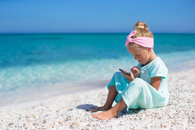 Pequeña muchacha adorable que juega en teléfono durante la playa imagen de archivo libre de regalías Pequeña muchacha adorable que juega en teléfono durante la playa imagen de archivo libre de regalías