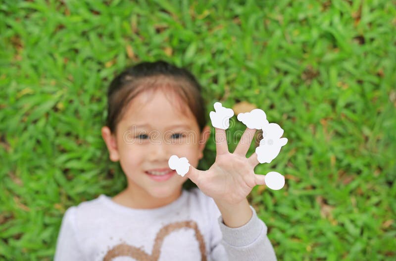 Pequeña muchacha asiática linda del niño que miente en césped de la hierba verde con las etiquetas engomadas blancas vacías de la imágenes de archivo libres de regalías Pequeña muchacha asiática linda del niño que miente en césped de la hierba verde con las etiquetas engomadas blancas vacías de la imágenes de archivo libres de regalías