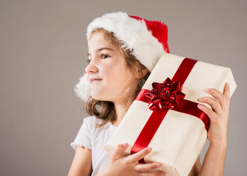 Pequeña muchacha en el sombrero de santa con el regalo de la Navidad imágenes de archivo libres de regalías Pequeña muchacha en el sombrero de santa con el regalo de la Navidad imágenes de archivo libres de regalías