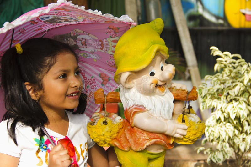 Pequeña muchacha india con la estatua de la historieta que sonríe mientras que sostiene el paraguas rosado dentro del jardín, fotos de archivo libres de regalías Pequeña muchacha india con la estatua de la historieta que sonríe mientras que sostiene el paraguas rosado dentro del jardín, fotos de archivo libres de regalías