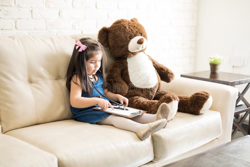Pequeña muchacha linda del doctor que juega con el oso de peluche imagen de archivo Pequeña muchacha linda del doctor que juega con el oso de peluche imagen de archivo