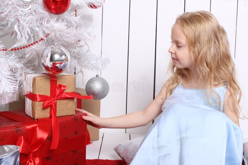 Pequeña muchacha linda que se sienta debajo del árbol y de las cajas de los controles con los regalos fotografía de archivo Pequeña muchacha linda que se sienta debajo del árbol y de las cajas de los controles con los regalos fotografía de archivo