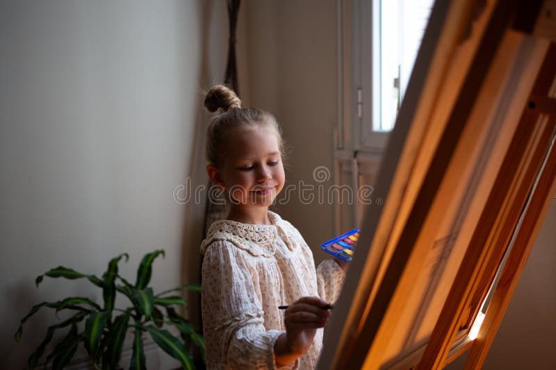 Pequeña niña linda dibuja con pinturas sobre lienzo en la comadreja. el concepto de desarrollo temprano de talentos infantiles. fotos de archivo libres de regalías
