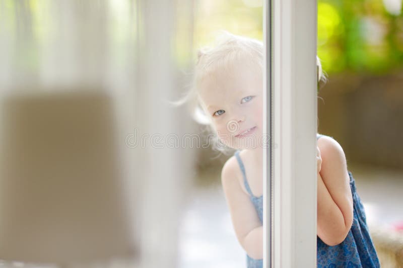 Pequeña niña pequeña linda que mira a escondidas en una ventana imágenes de archivo libres de regalías Pequeña niña pequeña linda que mira a escondidas en una ventana imágenes de archivo libres de regalías