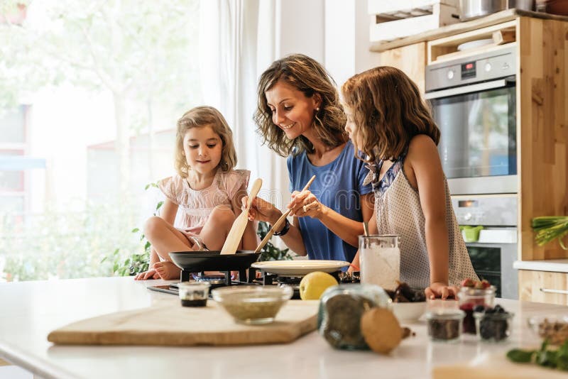 Pequeñas hermanas que cocinan con su madre en la cocina fotografía de archivo Pequeñas hermanas que cocinan con su madre en la cocina fotografía de archivo
