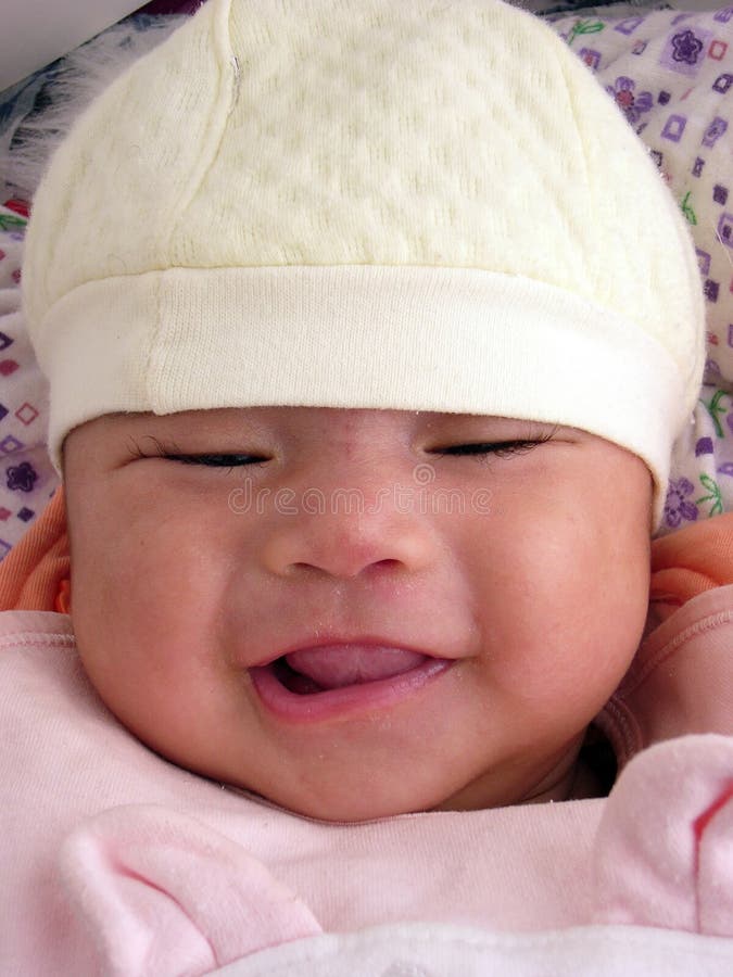 A little asian baby girl chuckling shyly with a yellow cap on head,dotted background. A little asian baby girl chuckling shyly with a yellow cap on head,dotted background
