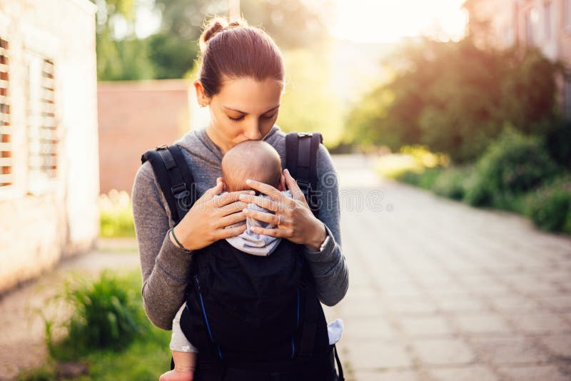 Pequeño bebé y su madre que caminan afuera durante puesta del sol La madre es que detiene y de cosquilleo de su bebé, babywearing imagenes de archivo Pequeño bebé y su madre que caminan afuera durante puesta del sol La madre es que detiene y de cosquilleo de su bebé, babywearing imagenes de archivo