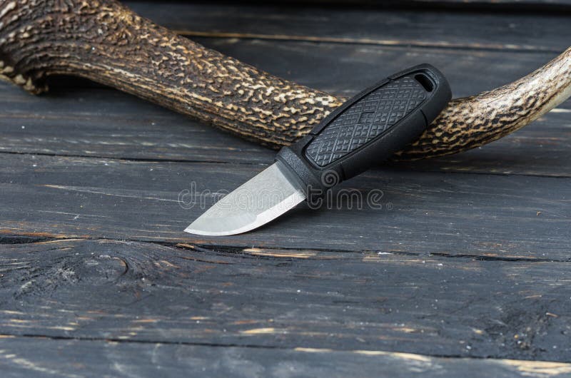 Pequeño cuchillo turístico en un fondo de madera negro con un cuerno del reno foto de archivo