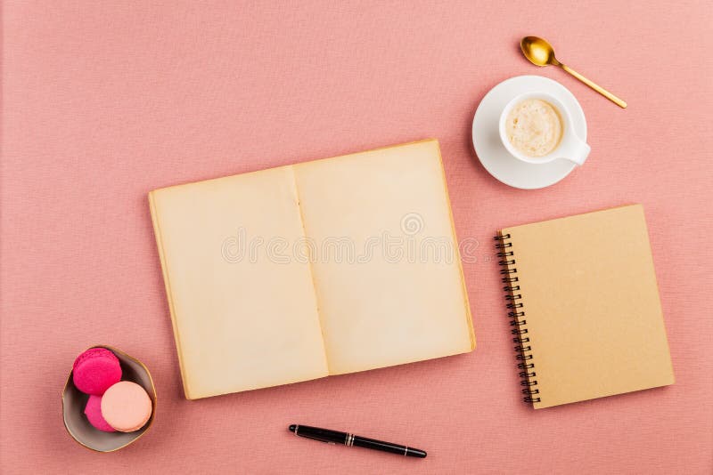 Pequeño libro antiguo vacío abierto con los macarrones franceses rosados en el lado, la taza de café, la cuchara de oro y el cuad fotos de archivo libres de regalías Pequeño libro antiguo vacío abierto con los macarrones franceses rosados en el lado, la taza de café, la cuchara de oro y el cuad fotos de archivo libres de regalías