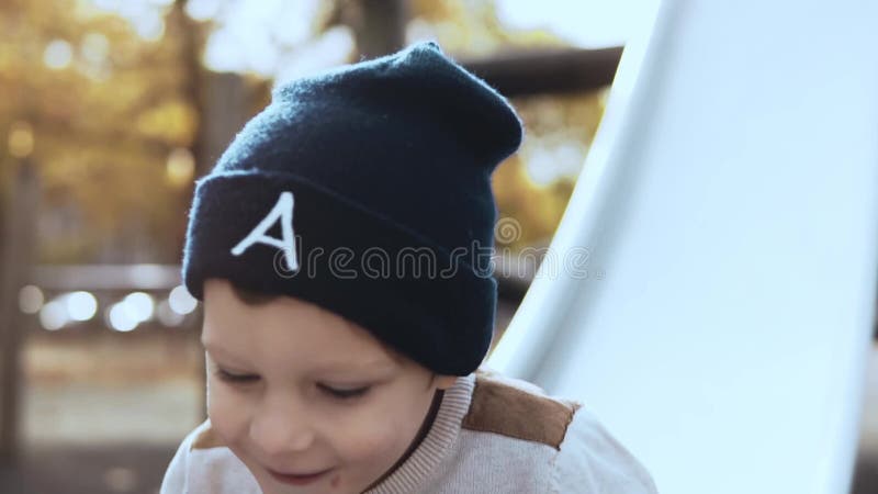 Pequeño muchacho europeo que va abajo de una diapositiva del parque Niño masculino despreocupado feliz en el sombrero que se divi almacen de metraje de vídeo