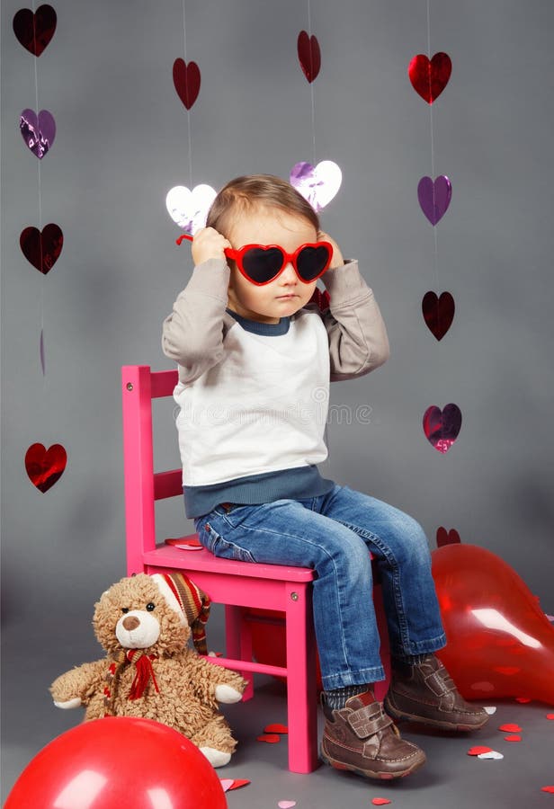 Pequeño niño del bebé que se sienta en pequeña silla rosada con el juguete del oso en el estudio que lleva los vidrios divertidos fotos de archivo libres de regalías Pequeño niño del bebé que se sienta en pequeña silla rosada con el juguete del oso en el estudio que lleva los vidrios divertidos fotos de archivo libres de regalías