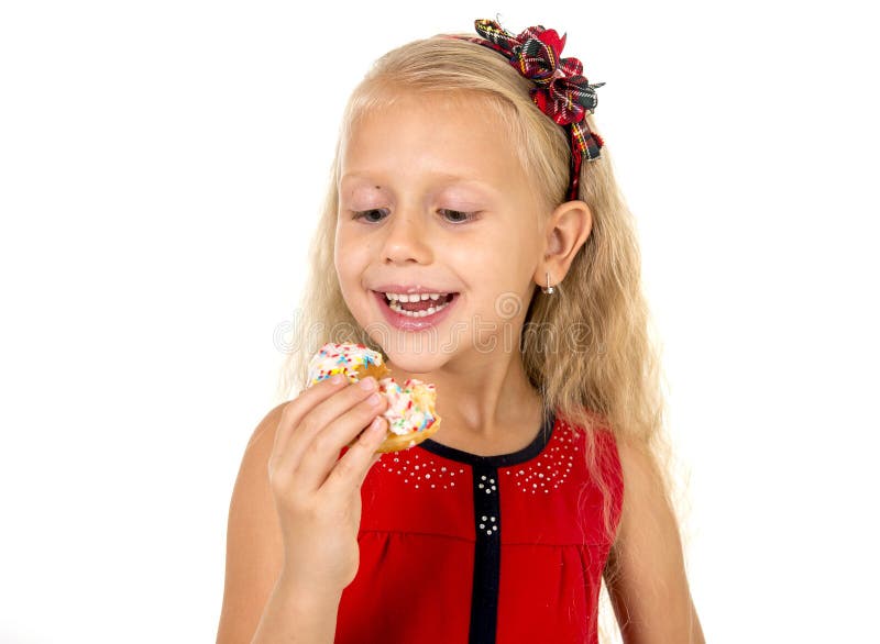 Little beautiful female child with long blonde hair and red dress eating sugar donut with toppings delighted and happy isolated on white background in children sweet and sugary nutrition. Little beautiful female child with long blonde hair and red dress eating sugar donut with toppings delighted and happy isolated on white background in children sweet and sugary nutrition