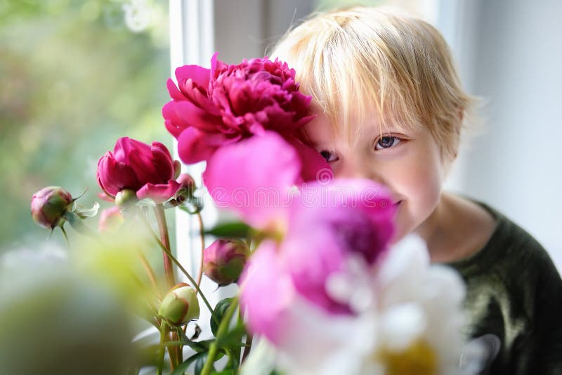 Cute little child and amazing bouquet of white and purple peonies. Beautiful flowers on window sill at home. Cute little child and amazing bouquet of white and purple peonies. Beautiful flowers on window sill at home