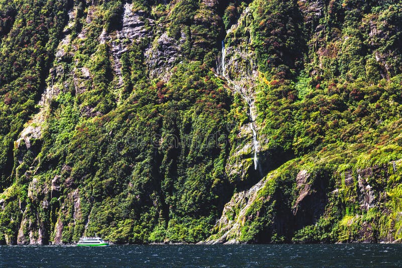 Pequeño transbordador de la travesía y alta cascada en Milford Sound, Nueva Zelanda imagen de archivo Pequeño transbordador de la travesía y alta cascada en Milford Sound, Nueva Zelanda imagen de archivo