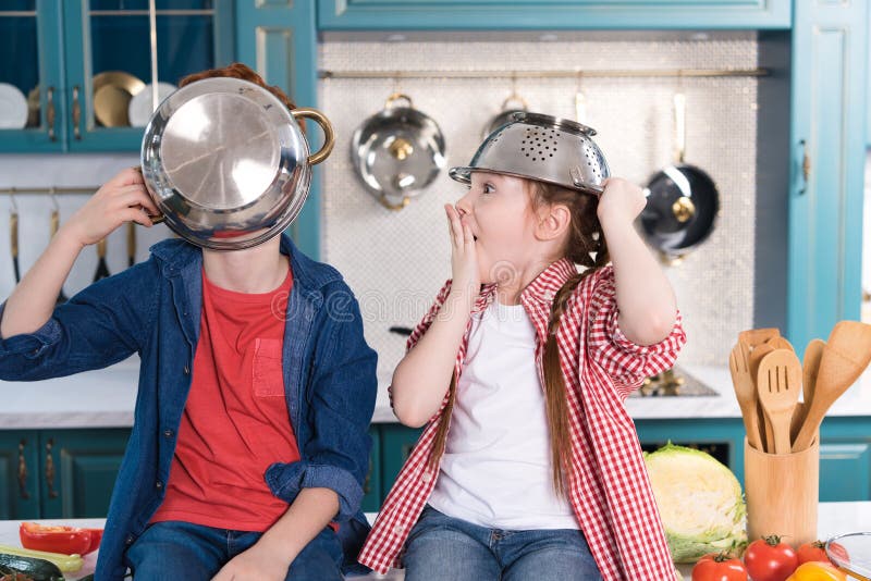 Pequeños niños adorables que se divierten con los utensilios mientras que se sienta en la tabla de cocina