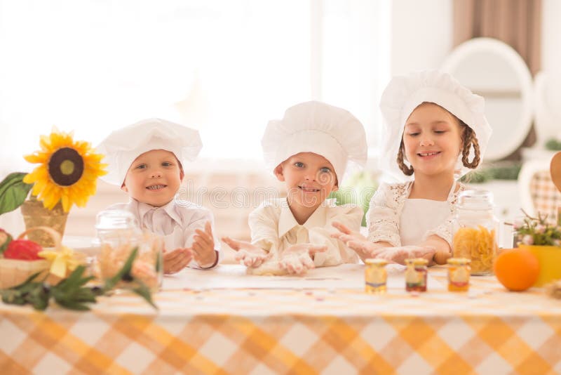 Pequeños niños felices bajo la forma de cocinero para cocinar un desayuno delicioso en la cocina imagen de archivo libre de regalías Pequeños niños felices bajo la forma de cocinero para cocinar un desayuno delicioso en la cocina imagen de archivo libre de regalías