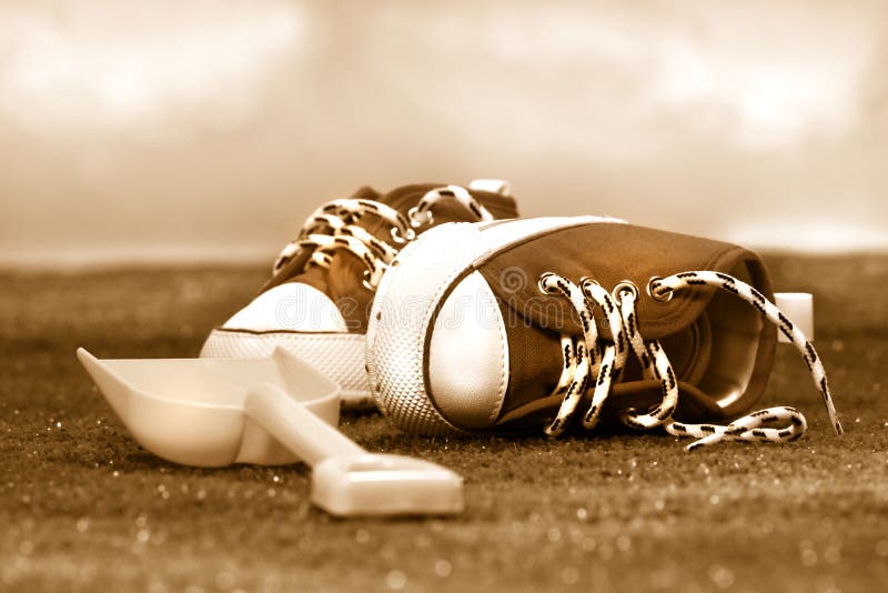 Little red running shoes and shovel on the grass/ Sepia tone. Little red running shoes and shovel on the grass/ Sepia tone