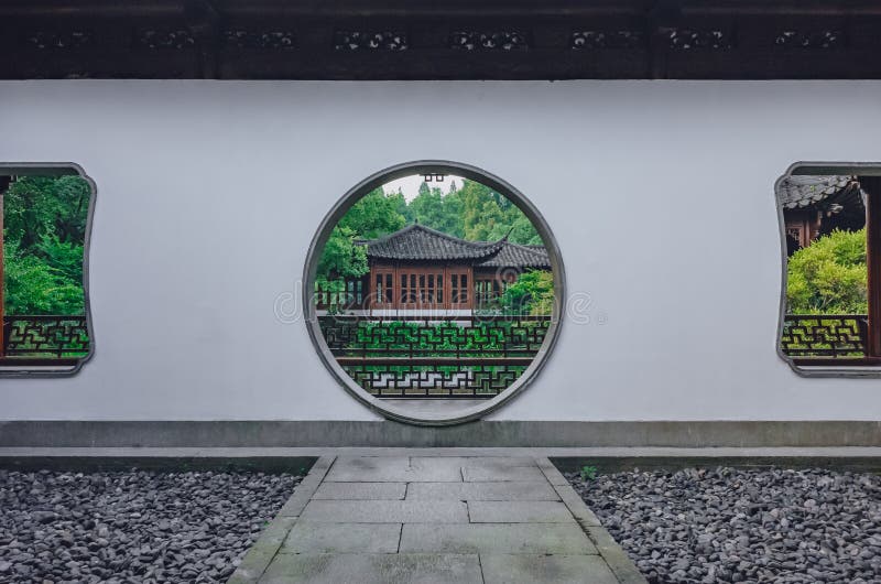 Percorso che conduce al portone della luna con la vista della costruzione del cinese tradizionale, in un giardino cinese, vicino fotografia stock Percorso che conduce al portone della luna con la vista della costruzione del cinese tradizionale, in un giardino cinese, vicino fotografia stock