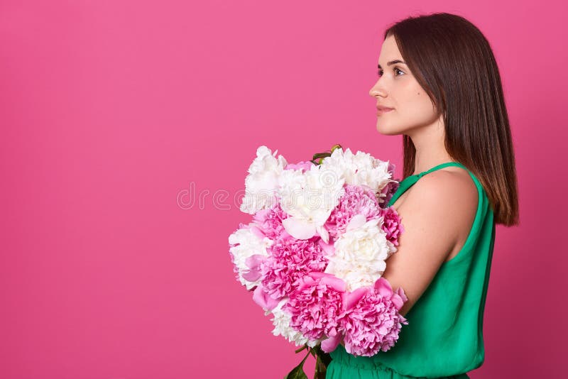 Perfil da mulher europeia atrativa pensativa que olha direta, guardando as flores, estando isoladas sobre o fundo cor-de-rosa imagem de stock Perfil da mulher europeia atrativa pensativa que olha direta, guardando as flores, estando isoladas sobre o fundo cor-de-rosa imagem de stock