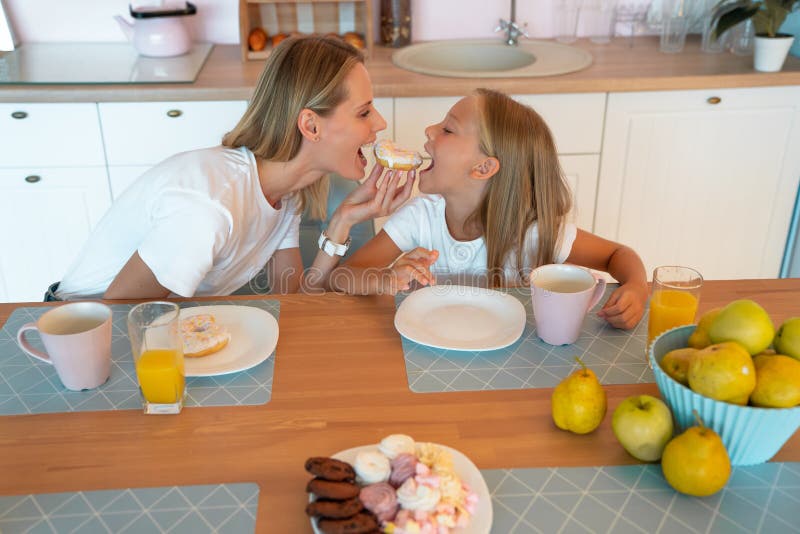 Perfil da mãe e da filha na cozinha mordendo a rosquinha em ambos os lados fotografia da família fofa vestida com camisas brancas foto de stock Perfil da mãe e da filha na cozinha mordendo a rosquinha em ambos os lados fotografia da família fofa vestida com camisas brancas foto de stock
