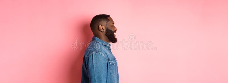 Perfil de un guapo negro barbudo parado sobre fondo rosado sonriendo y mirando a la izquierda en el espacio de copia fotografía de archivo libre de regalías