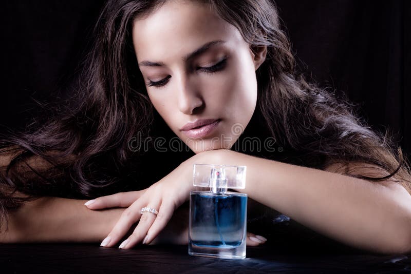 Donna con una bottiglia di profumo, studio sfondo scuro.