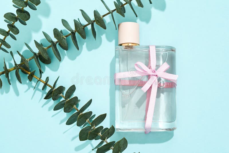 Perfume Bottle with Bow and Green Leaf Branches on Blue Background
