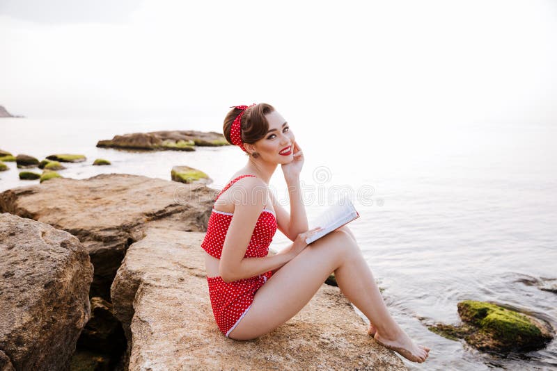 Perno sorridente sul libro di lettura della ragazza che si siede sulla roccia fotografia stock Perno sorridente sul libro di lettura della ragazza che si siede sulla roccia fotografia stock