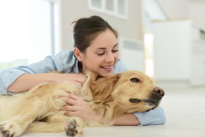 Perro que acaricia de la mujer joven en el piso imagen de archivo Perro que acaricia de la mujer joven en el piso imagen de archivo