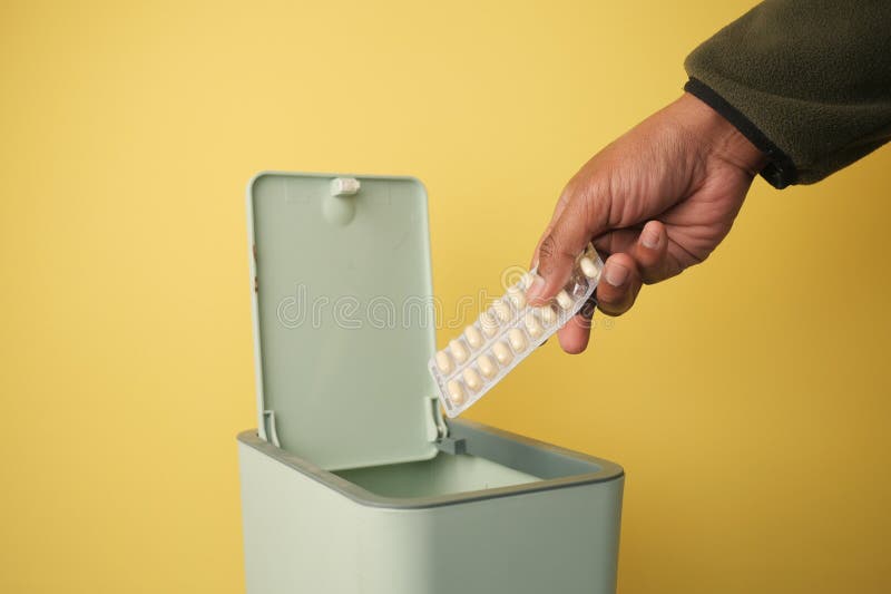Disposing of medication in a green trash bin against yellow background stock photos