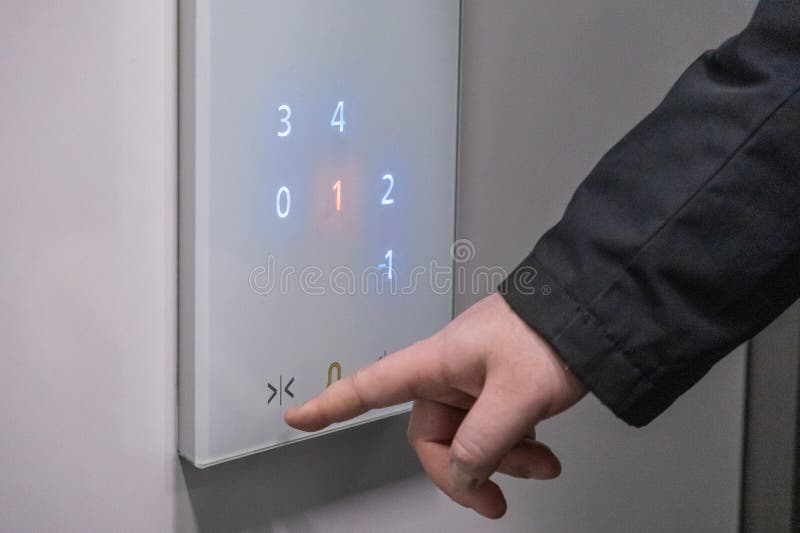 Person drückt auf modernem Fahrstuhl-Bedienfeld mit beleuchteten Bodennummern und minimalistischer Schnittstelle auf Knopfdruck stockbild