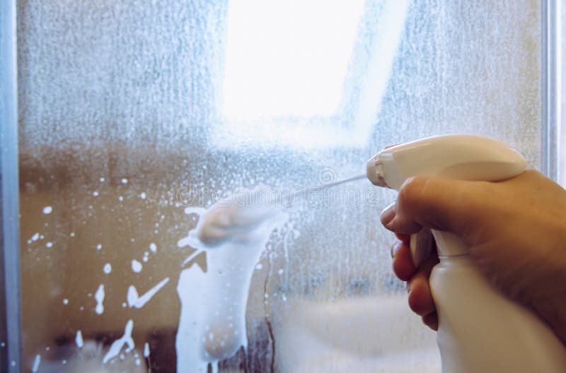 Person hand using limescale remover chemical foam. Descaling shower case glass door. stock image