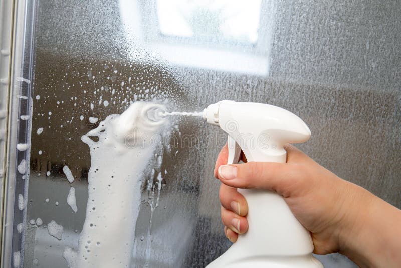 Person hand using limescale remover chemical foam. Descaling shower case glass door. Work in progress. royalty free stock photo