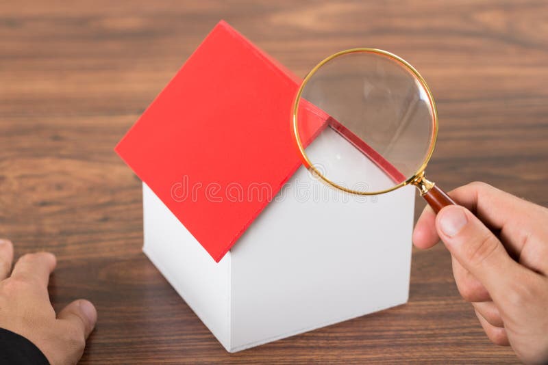 Person hands with magnifying glass and model house