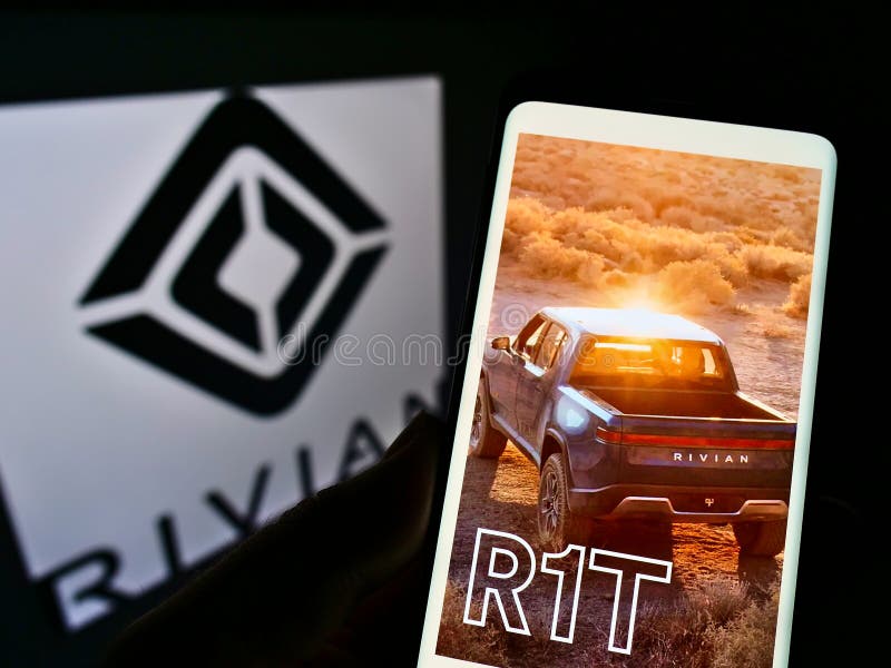 Person holding cellphone with web page of US electric vehicle company Rivian Automotive on screen in front of logo.