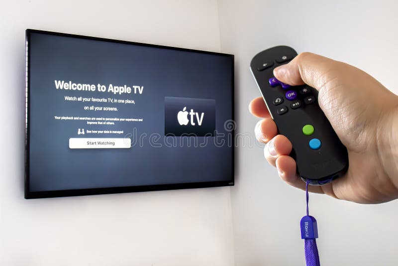 A person holding a Roku remote control with the apple tv application open on a screen tv background