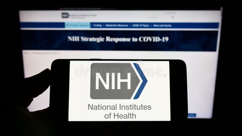 Person holding smartphone with logo of US agency National Institutes of Health (NIH) on screen in front of website. royalty free stock image Person holding smartphone with logo of US agency National Institutes of Health (NIH) on screen in front of website. royalty free stock image