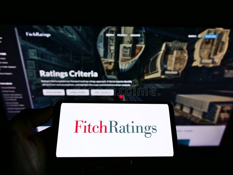 Person holding smartphone with logo of US credit rating agency Fitch Ratings Inc. on screen in front of business website.
