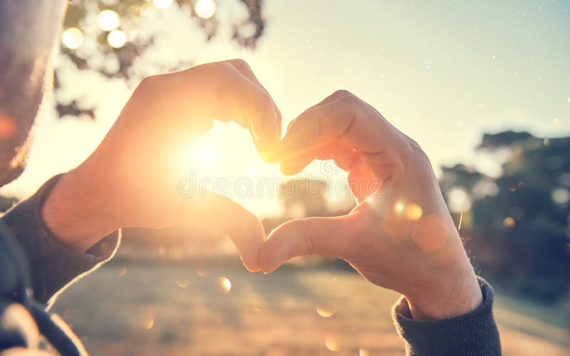 Person making heart with hands over nature sunset background. Happy young people. Silhouette hand in heart shape with sun inside. Vacation, environment concept. Summer holidays