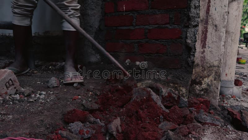 Person mit einer Metallstange, die an einer Baustelle arbeitet, die Ziegel und Schutt baut