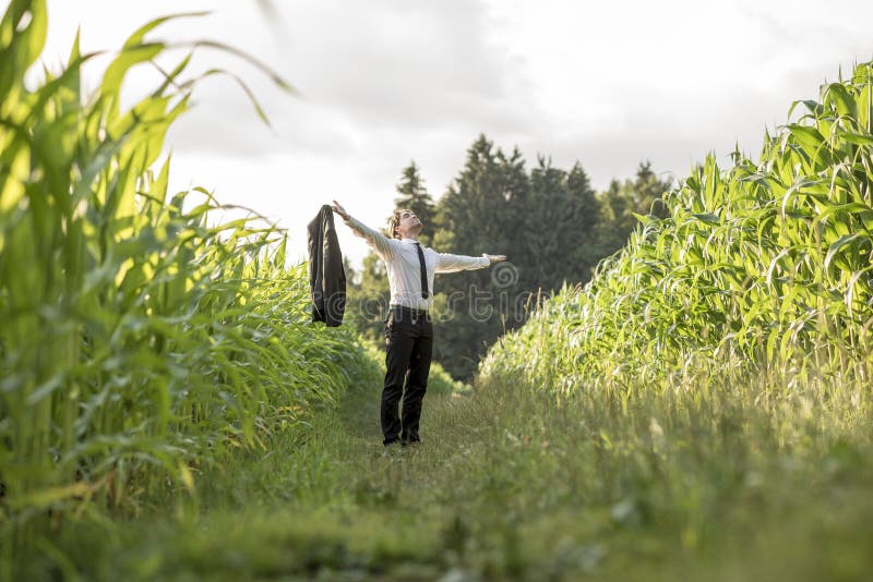 Person in necktie standing in between rows of corn