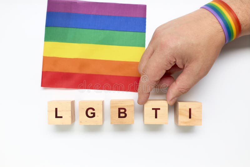 Person placing letter blocks forming the word LGBTI next to the rainbow flag on a white background royalty free stock photo Person placing letter blocks forming the word LGBTI next to the rainbow flag on a white background royalty free stock photo