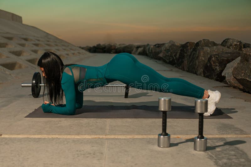 Person som deltar i plank vid träning av träningsbalkar nära strandlinje under tidig morgon. Vatten och berg för stillastående arkivfoton