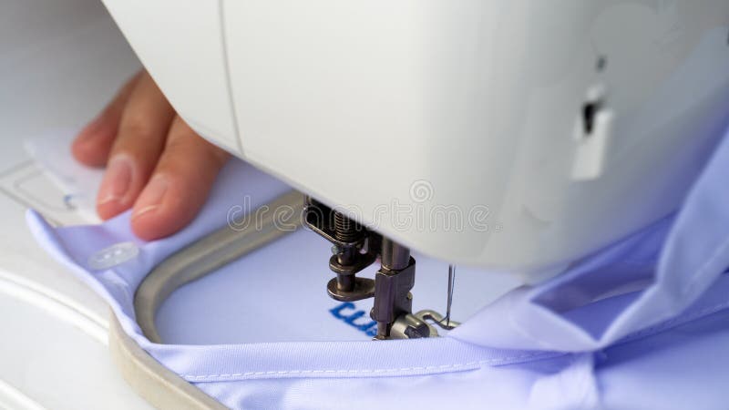 Person som leder ljusblå tyg under nålen på en vit broderimaskin. arkivfoto