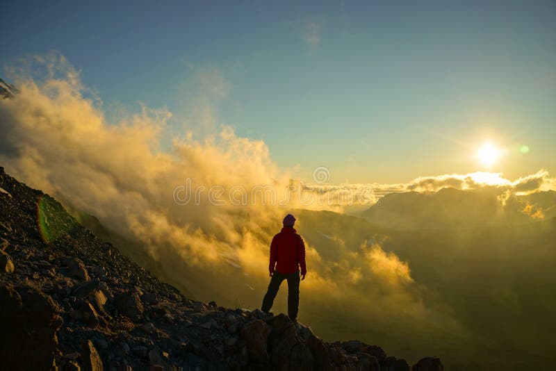 A hiker is standing on the mountain with clouds during sunset/sunrise at Mount Rainier National Park, Washington. A hiker is standing on the mountain with clouds during sunset/sunrise at Mount Rainier National Park, Washington.