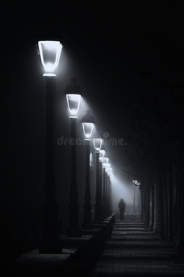 Person walking on dark street illuminated with streetlamps