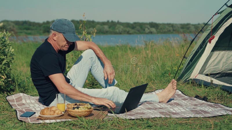 A man works on a computer sitting in nature.
